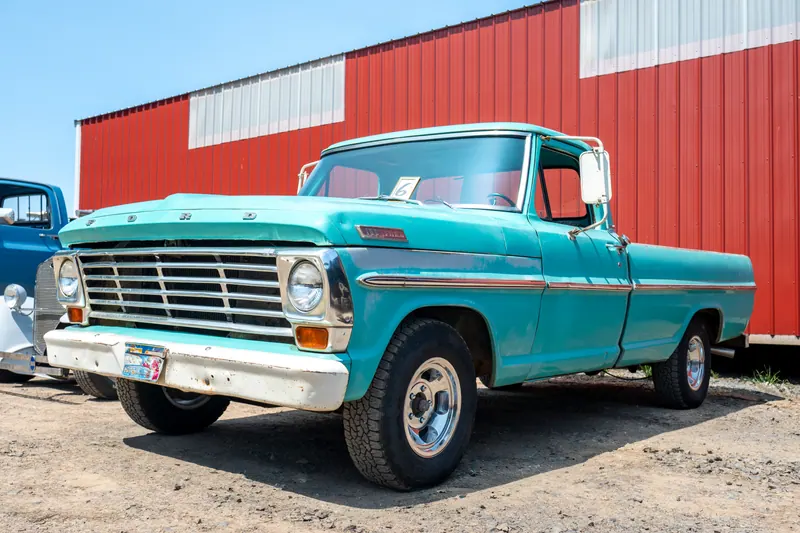 Turquoise and white classic pickup truck photographed three-quarter front against red barn siding