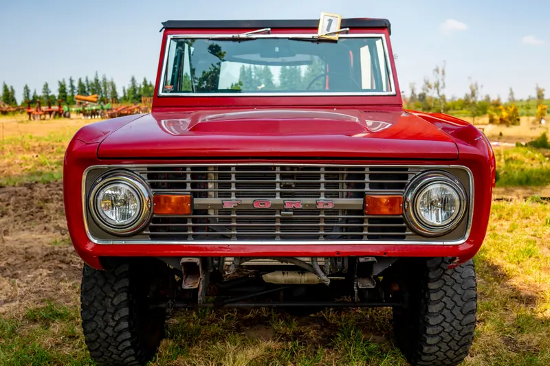 Head-on view of a red vintage four-wheel-drive with round headlights and a chrome grille, parked in dry grass