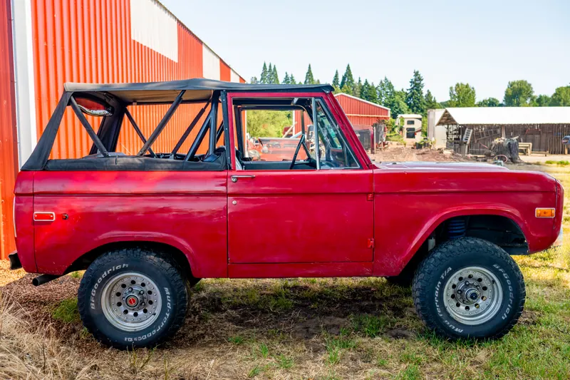 Side profile of the red four-wheel-drive with its soft top up, white wheels and knobby tyres