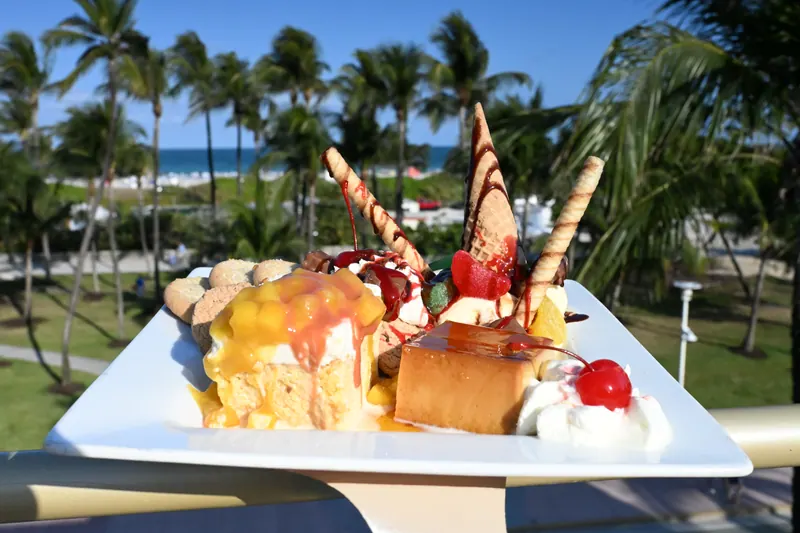 Tropical dessert platter with waffle cones, fresh fruit and whipped cream, photographed outdoors with palm trees and the ocean behind