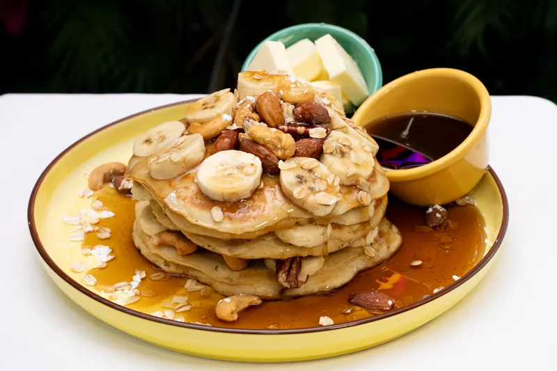 Stack of banana nut pancakes with syrup and a pot of caramel sauce on a yellow plate