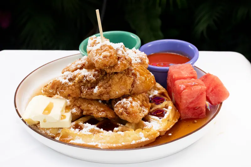 Fried chicken over waffles dusted with sugar, served with watermelon and small bowls of sauce