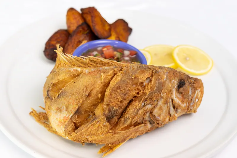 Whole crisp-fried fish plated with sweet plantains, a bowl of beans and a lemon wedge