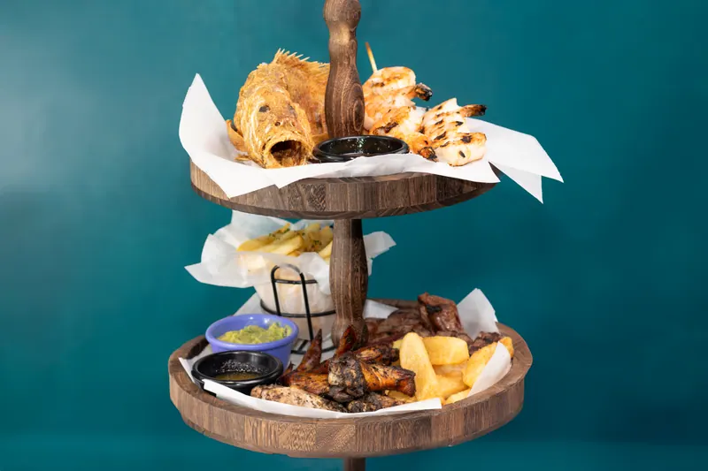 Three-tier wooden seafood tower with rolls, skewers and dipping sauces against a deep teal background
