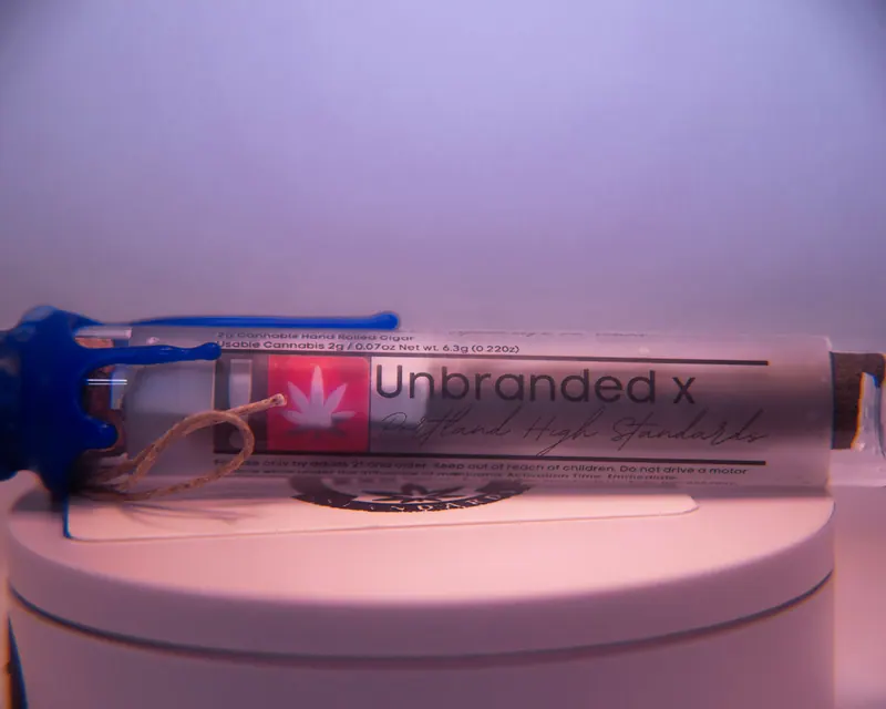 Single product tube with a blue wax seal resting on a pale rounded pedestal, soft high-key lighting